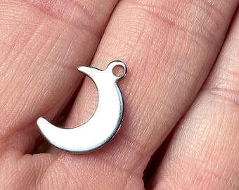 May include: A silver crescent moon charm with a small hole at the top for attaching to a necklace or bracelet.