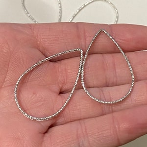 May include: Two silver teardrop-shaped earring blanks with a textured surface.