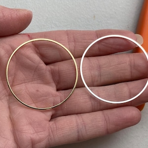 May include: Two hoop earrings, one gold and one silver, on a hand.