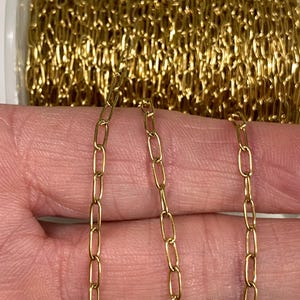 May include: Close-up of gold-colored chain links. The chain is in a roll, with a few strands extended. The links are oval-shaped and appear to be made of metal. The chain is held by a person.