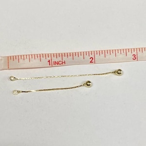May include: Two gold chain extenders with small round balls at the end. The extenders are about 1 inch long and are measured against a ruler.