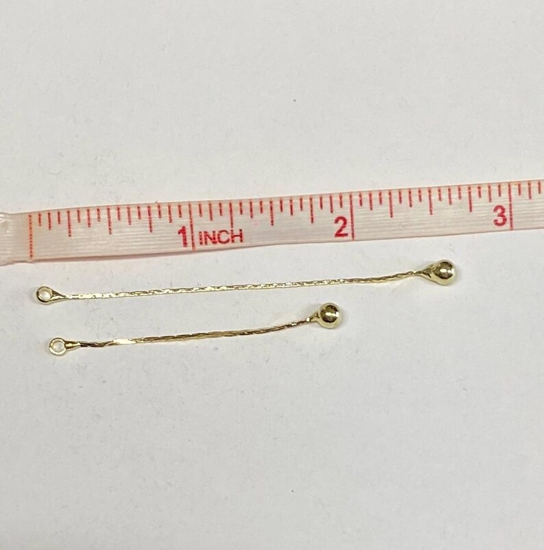 May include: Two gold chain extenders with small round balls at the end. The extenders are about 1 inch long and are measured against a ruler.