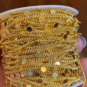 May include: A spool of gold chain trim with small round discs attached. The chain is coiled and the discs are visible on the outside of the coil.