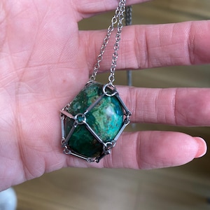 May include: A silver chain necklace with a green gemstone pendant encased in a silver cage.