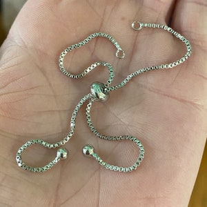 May include: A silver chain bracelet with a sliding clasp and two small round beads.