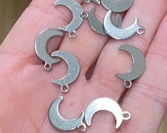 May include: A collection of small, silver-colored metal moon charms, each featuring a smooth, crescent-shaped design with a single circular jump ring attached at the bottom for hanging, presented in a group of seven individual pieces.