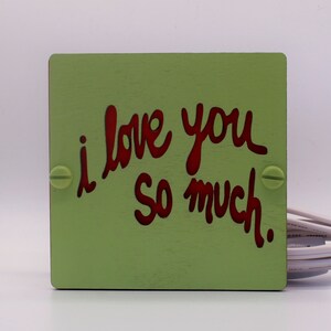 May include: A green wooden sign with the words "i love you so much" written in red.