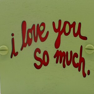 May include: A light green wooden sign with the words "i love you so much" written in red.