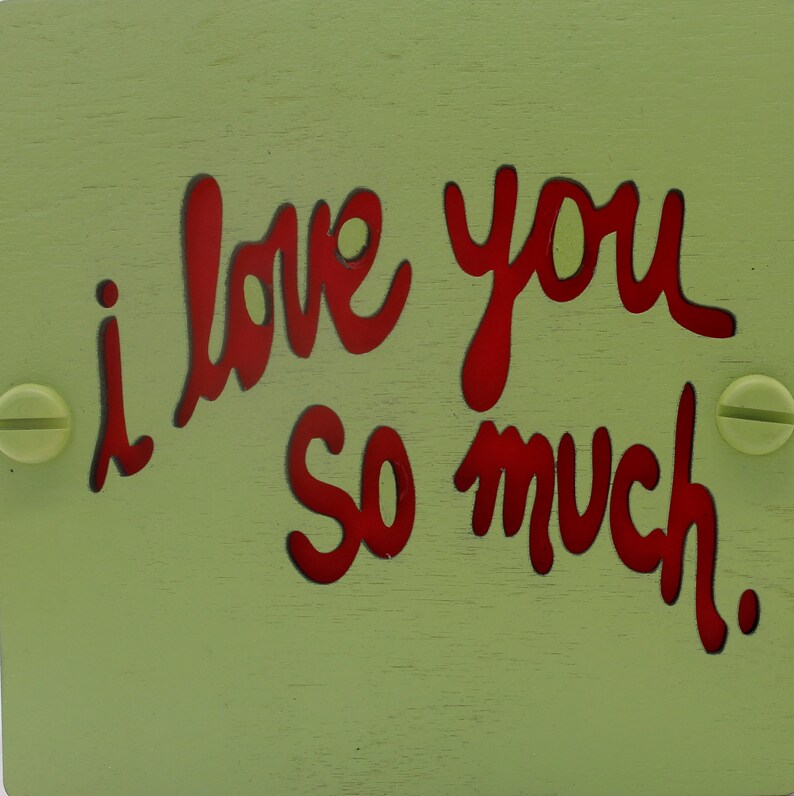 May include: A light green wooden sign with the words "i love you so much" written in red.