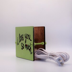 May include: A green wooden box with a message that says "I love you so much." The box is attached to a brown wooden box with a white electrical cord.