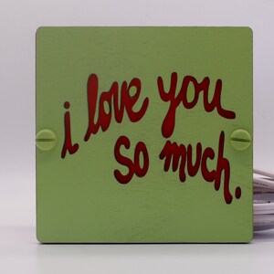 May include: A green wooden sign with the words "i love you so much" written in red.