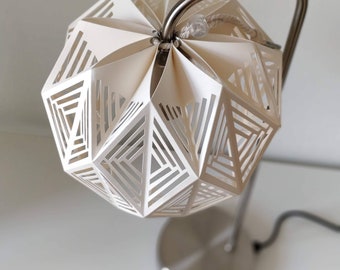 Könnte beinhalten: Ein weißer geometrischer Lampenschirm mit einem silbernen Metallfuß und Arm. Der Lampenschirm ist aus Papier gefertigt und hat ein ausgeschnittenes Design.