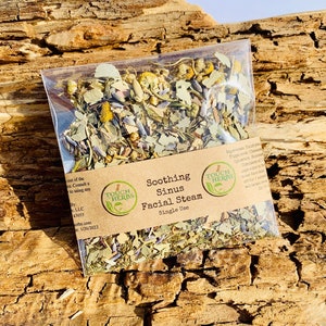 May include: A clear plastic packet filled with dried herbs for facial steam, labeled "Soothing Sinus Facial Steam." The packet is set against a textured, light brown wooden surface. The label includes the brand name "Touch Herbs."