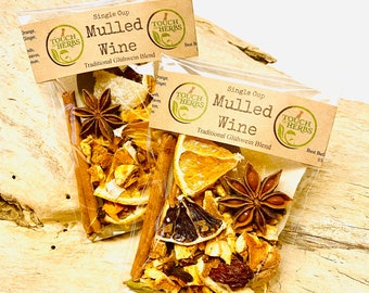 May include: Two sachets of mulled wine spices, containing star anise, cinnamon, and dried orange. The packaging reads "Mulled Wine" and "Traditional Glühwein Blend". The sachets are presented on a light-toned wooden surface, ideal for festive drinks.