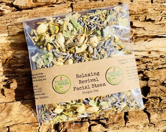 May include: A clear plastic packet filled with dried herbs, labeled "Relaxing Revival Facial Steam." The packet contains a mix of lavender, white flower buds, and green leaves. The background is a piece of textured, light brown wood.