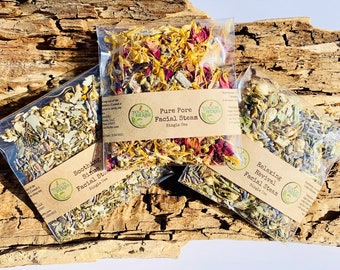 May include: Three clear packets of facial steam, each filled with dried herbs and flowers. The packets are labeled "Soothing Sinus", "Pure Pore", and "Relaxing Revival". The background is a piece of weathered wood.