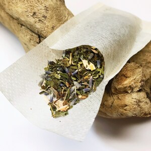 Peut inclure: Un sachet de th&eacute; blanc rempli d'un m&eacute;lange d'herbes et de fleurs s&eacute;ch&eacute;es, dont de la lavande et de la menthe. Le sachet de th&eacute; est ouvert, r&eacute;v&eacute;lant le contenu color&eacute;. Le sachet de th&eacute; repose sur un morceau de bois flott&eacute; sur fond blanc.