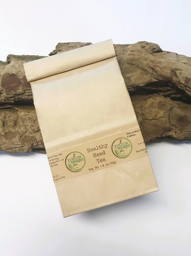 Peut inclure: Un sachet en papier beige de "Healthy Head Tea" avec une &eacute;tiquette marron et un logo vert. L'&eacute;tiquette indique "Net. Wt. 50g". Le sachet est pos&eacute; sur un morceau de bois flott&eacute;.