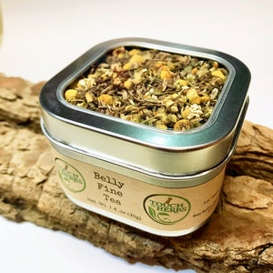 May include: A square, silver tin of Belly Fine Tea, filled with dried herbs and flowers. The label reads "Touch of Herbs" and "Net Wt. 1.4 oz (40g)". The tin sits on a piece of wood.