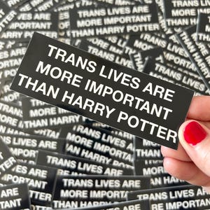 May include: A close-up of a stack of black and white stickers with the text "Trans Lives Are More Important Than Harry Potter".