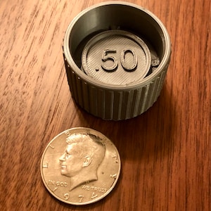 May include: A silver-colored coin with the number .50 printed on it. The coin is inside a silver-colored container with a ribbed edge.