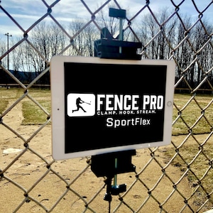 Może przedstawiać: Biały tablet jest zamontowany na ogrodzeniu z siatki drucianej za pomocą czarnego zacisku. Na tablecie widnieje napis "FENCE PRO" z sylwetką gracza w baseball i słowami "CLAMP. HOOK. STREAM. SportFlex."