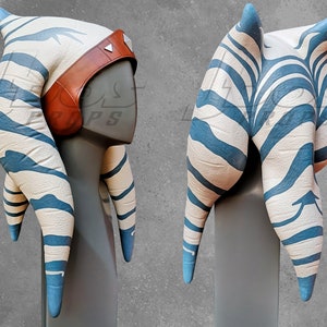 May include: A white and blue striped headdress with a brown leather band. The headdress is made of fabric and has a pointed top. It is a replica of a headdress worn by a fictional character.