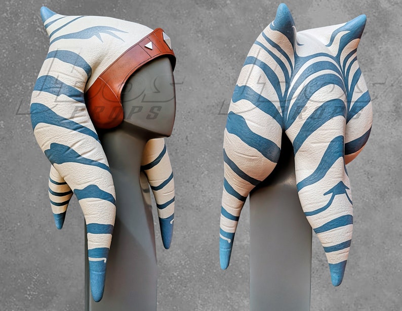 May include: A white and blue striped headdress with a brown leather band. The headdress is made of fabric and has a pointed top. It is a replica of a headdress worn by a fictional character.