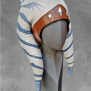 May include: A white and blue striped headdress with a brown leather band and silver accents. The headdress is on a gray mannequin head.