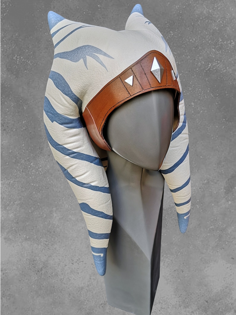 May include: A white and blue striped headdress with a brown leather band and silver accents. The headdress is on a gray mannequin head.