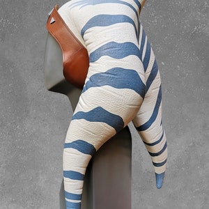 May include: A white and blue striped headpiece with a brown leather strap. The headpiece is shaped like two horns and is designed to resemble a Twi'lek head.