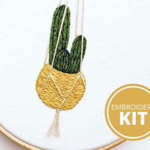 Op de afbeelding: Borduurset met een hangende potcactus met groene bladeren en een gele pot. De set bevat alle materialen die nodig zijn om het borduurpatroon te maken. De afbeelding bevat ook de tekst "EMBROIDERY KIT".