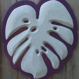 May include: A white, textured, carved monstera leaf with a purple outline. The leaf is shaped like a heart and has a raised, three-dimensional design.
