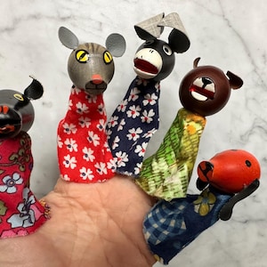 May include: A hand displays five vintage finger puppets. Each puppet has a painted wooden head and a fabric body. The puppets include a black horse, a gray mouse, a black and white donkey, a brown bear, and a red ladybug.