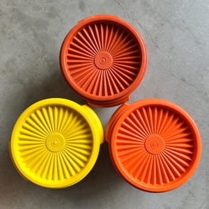 Peut inclure: Trois couvercles de récipients de stockage ronds en plastique disposés en triangle. Un couvercle est jaune vif et deux couvercles sont orange vif. Chaque couvercle présente un motif en rayons partant du centre vers le bord extérieur.