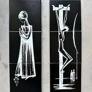 May include: Two black ceramic tiles with white line art. One tile shows a figure in a long dress, the other depicts a crucifixion scene. The tiles are likely part of a larger set, suitable for wall decor.