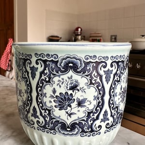 May include: Large, round ceramic planter with a blue and white floral design. The planter features a detailed pattern of flowers and leaves against a white background. The rim and base have a light blue accent.
