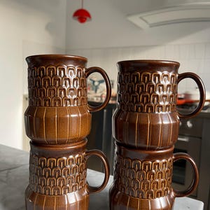 May include: Set of four brown ceramic mugs with a geometric pattern. The mugs are stacked in pairs.
