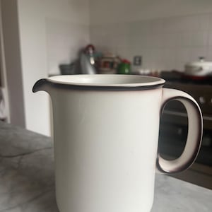 May include: A white ceramic pitcher with a brown rim and handle. The pitcher is empty and has a smooth, rounded shape.