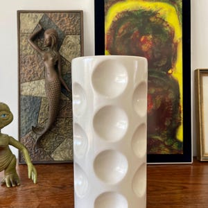 Peut inclure: Un vase en céramique blanche avec un motif texturé circulaire. Le vase est haut et cylindrique.