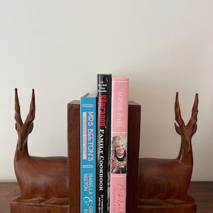 May include: A set of wooden deer bookends with a collection of cookbooks. The books include "Miss Sahl's Voluptuous Delights", "SonFanos Family Cookbook", and "Mrs. Beeton's Homemade Sweet Shop".