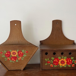 Peut inclure: Deux boîtes de rangement murales en bois avec des motifs floraux. La boîte de gauche est un porte-courrier de forme triangulaire. La boîte de droite a une forme rectangulaire avec six trous à l'avant.