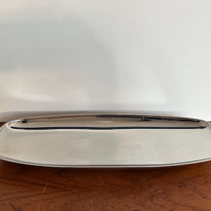 Könnte beinhalten: Ein poliertes, silberfarbenes Serviertablett mit rechteckiger Form und abgerundeten Ecken. Das Tablett hat eine reflektierende Oberfläche und steht auf einer Holzoberfläche. Das Tablett ist zum Servieren von Speisen oder zum Präsentieren von Gegenständen bestimmt.