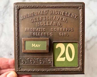 Antieke eeuwigdurende kalender van de J.H. Henkes Distillery in Delfshaven, Nederland, met daarop hun 'Aromatic Schnapps Hollands Gin' blikje. ZELDZAAM