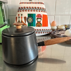 Könnte beinhalten: Ein Set aus drei Keramikbechern mit gesprenkelter, matter Oberfläche. Die Becher sind in Creme-, Hellgrau- und Dunkelgrautönen gehalten. Jede Tasse hat ein schlichtes, minimalistisches Design.