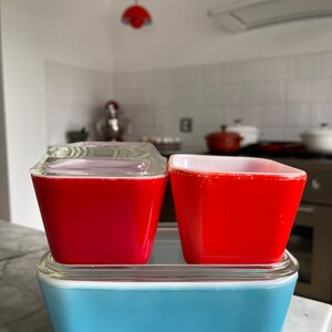 Peut inclure: Trois récipients de stockage en verre Pyrex vintage. Les deux du haut sont carrés et rouges, et celui du bas est rectangulaire et bleu.