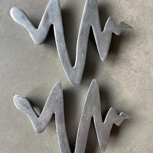 Può includere: Due sculture astratte in metallo argentato a forma di linea ondulata. Le sculture sono simili nella forma e nelle dimensioni.