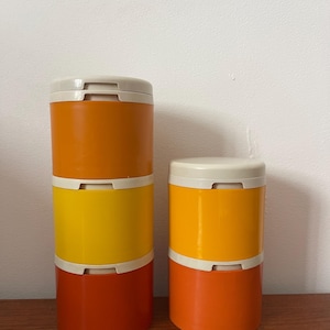 Op de afbeelding: Set van drie oranje, gele en witte plastic containers met deksels. De containers zijn op elkaar gestapeld.