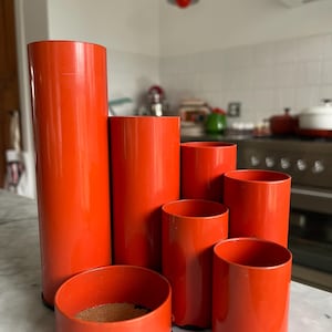 Pode incluir: Um conjunto de seis organizadores de mesa laranja feitos de metal. Os organizadores são de diferentes tamanhos e formas, e estão dispostos em um padrão escalonado. Os organizadores estão sobre uma superfície de mármore branco.
