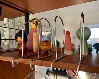 May include: A set of five silver metal bookends with a variety of colorful figurines, including a pink and white doll, a brown and white dog, a pink and red ghost, a green and white alien, and a blue and white bird.